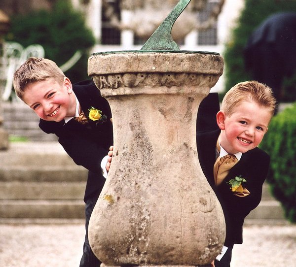 Picture of two young boys at a wedding looking out from behind a sundial by Jill Pendleton